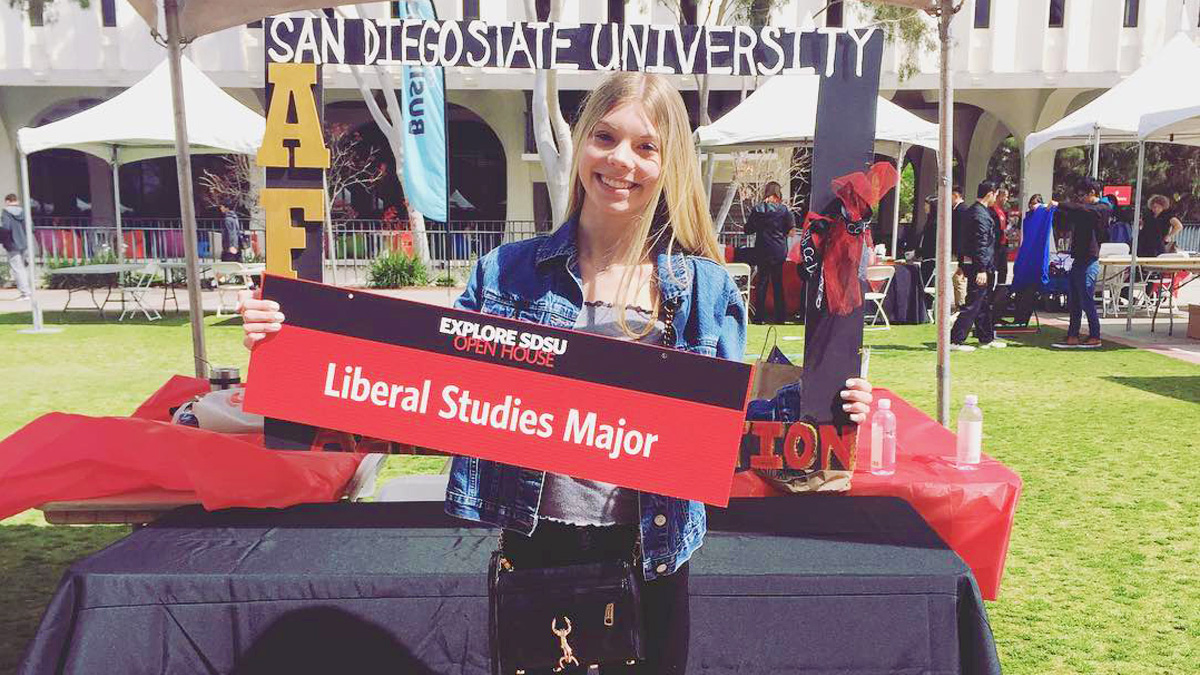 Liberal Studies student at career event smiling and holding up program sign