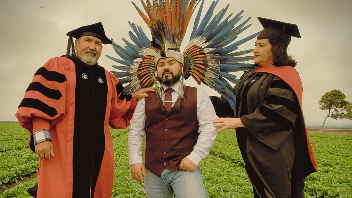Eric Becerra (center) wears his Aztec dancer headdress, while his parents don the doctoral regalia.
