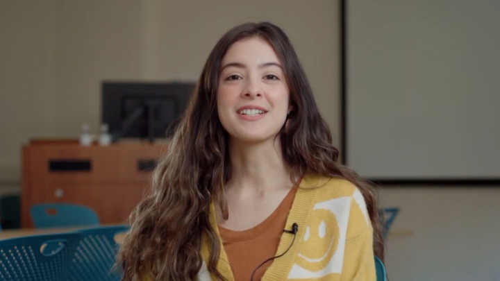 A smiling Alexia Herrera wearing a yellow sweater sit in a classroom