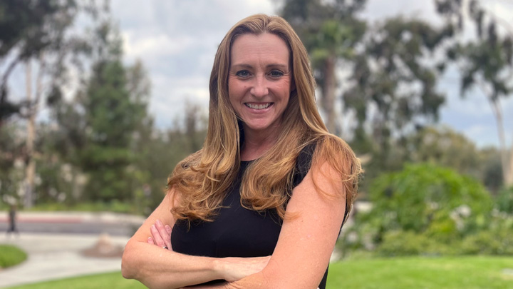 A woman wearing black smiles in front of a lush green background.