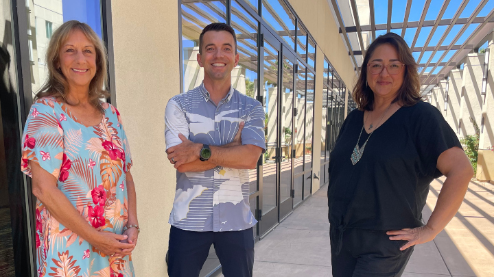 Three smiling professors pose outdoors.