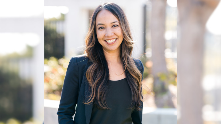 A woman in black smiles in an outdoor setting.