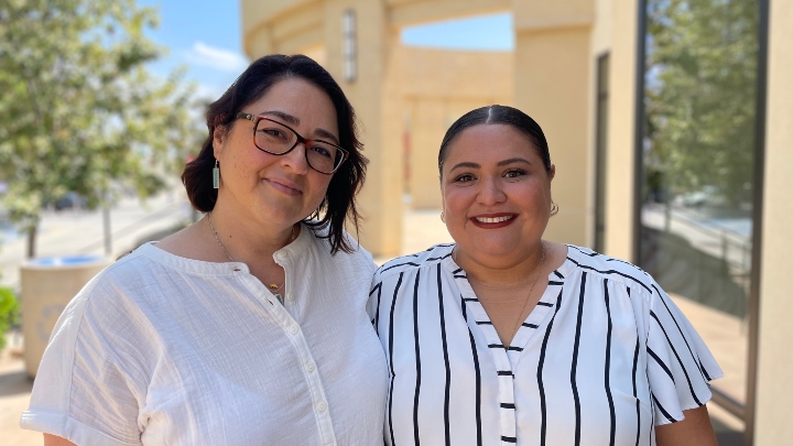 Two woman in white stand in front of a building entrance.