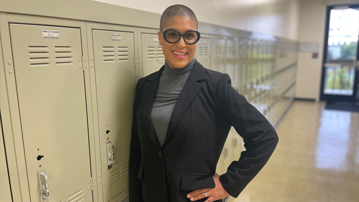 A woman in black smiles while leaning against a wall of lockers.