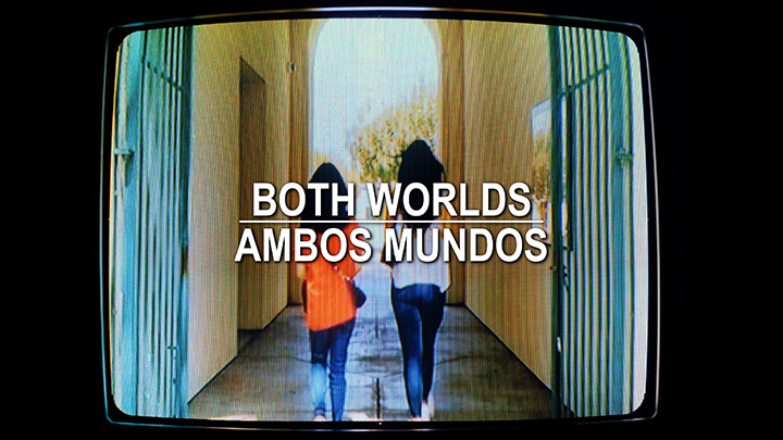 Two women walk through a gate with the title BOTH WORLDS/AMBOS MUNDOS in the foreground.