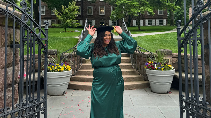 A woman in a green dress smiles while doffing a graduation cap.