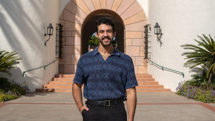 A man in a blue shirt stands in front of a white building.