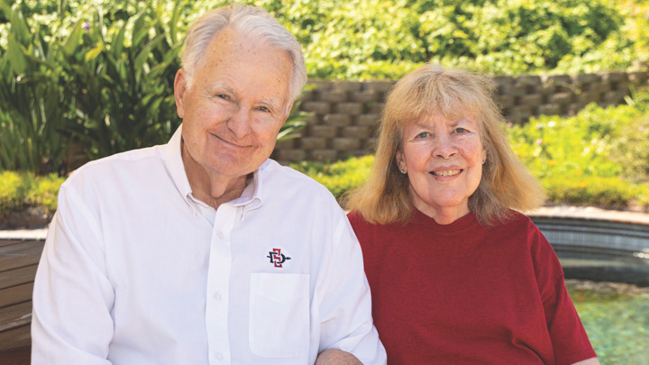 A man in white and a woman in red smile in front of a green backdrop.