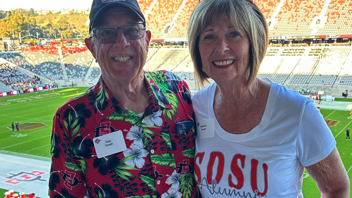 A man and woman smile posing at a football stadium.