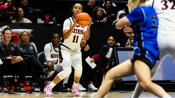 A basketball player in a white AZTECS uniform lines up a shot during a game.