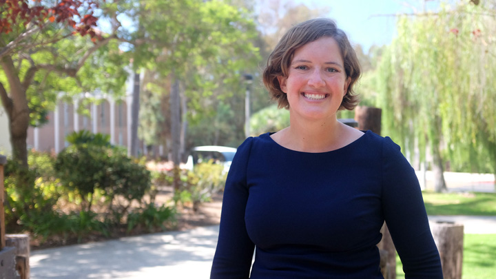 A woman in a blue shirt smiles against a green backdrop