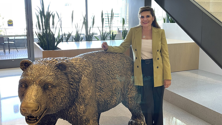 A woman in a blazer stands next to a bear statue