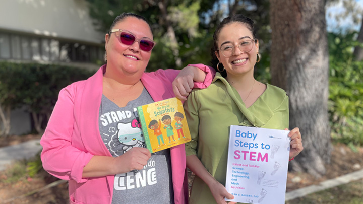 Two women smile while holding STEM children's books.