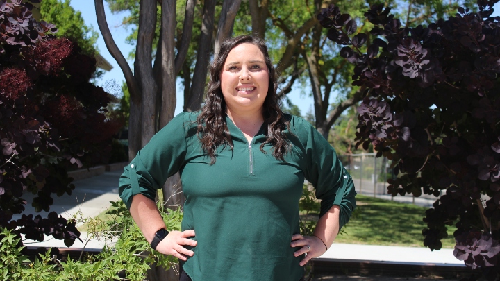 A woman in green smiles in front of a green backdrop.