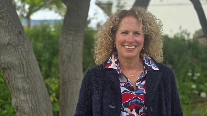 A woman in a blue blazer smiles in front of green backdrop.