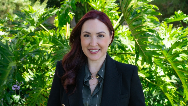 A woman in a black blazer smiles in front of a green backdrop.