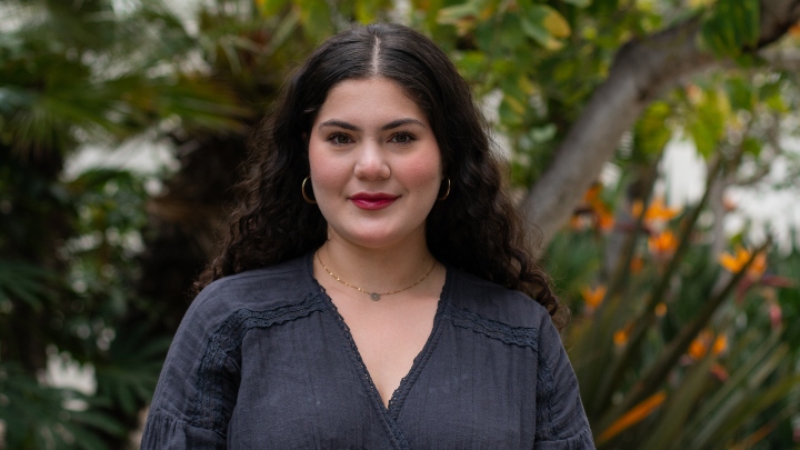 A woman in blac smiles in front of a green backdrop.