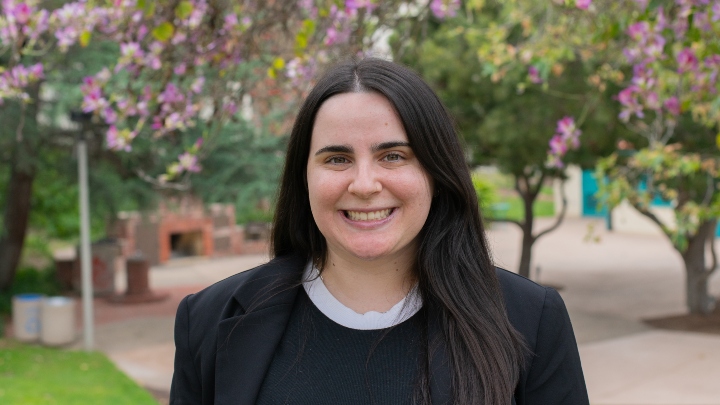 A woman in a black blazer smiles in front of a green background.