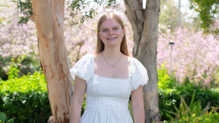A woman in white smiles in front of floral background.