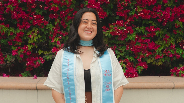 A woman in white smiles in front of a floral backdrop.