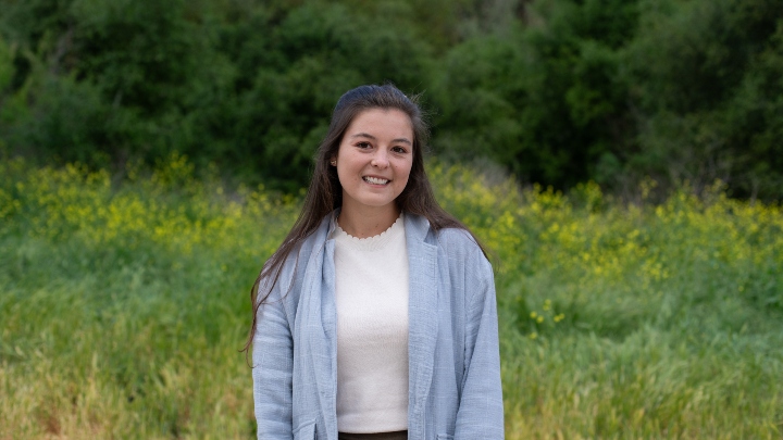 A woman in a blue cardigan smiles in front of a green backdrop.