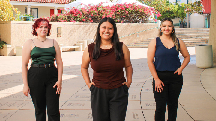 Three students stand in power poses in front of a library.