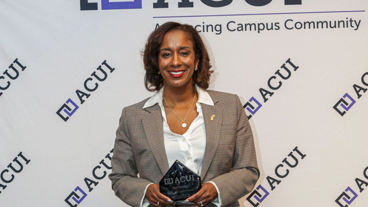 A woman in a beige blazer smiles while holding an award.