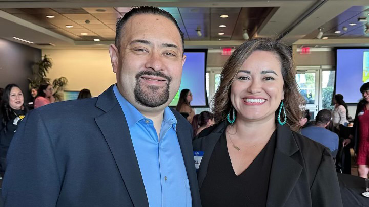 A man in blue and a woman in black smile at a book event.