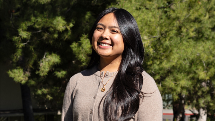 A woman in a beige sweater smiles in front of a green backdrop.