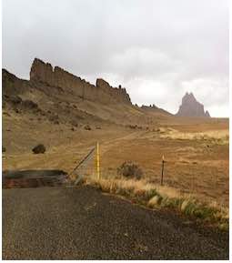 Shiprock scene with fence and road in foreground, mesa in background
