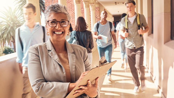 smiling teacher with clipboard in school walkway